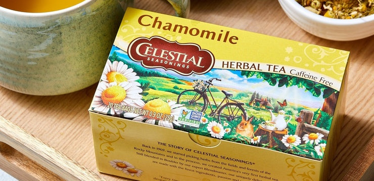 Celestial Seasonings Chamomile Herbal Tea box shown on a wooden surface with a green ceramic mug and a small bowl in the background.