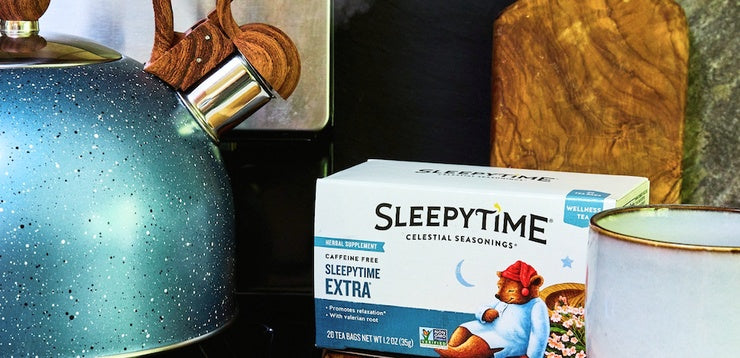 A box of Sleepytime Caffeine Free Sleeptime Extra tea placed on a kitchen counter next to a speckled teal kettle and a white mug.